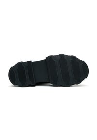 Semelle de chaussure en caoutchouc noir avec surface texturée, présentant des nervures et des rainures distinctes pour une meilleure adhérence. Design ergonomique avec un profil plat.