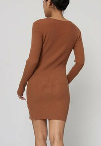 Robe à manches longues à côtes de couleur marron riche, avec une coupe ajustée et des fentes sur les côtés à l'ourlet. Texture lisse mettant en valeur une silhouette élancée.