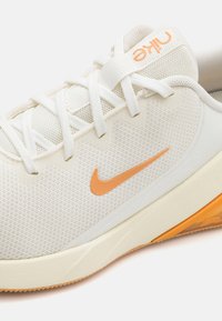Nike sportiniai batai su kreminiu tinkleliu, oranžiniu Swoosh logotipu, tekstūruotais akcentais ir guminiais padu, kuriame yra oranžinė detalė kulne.
