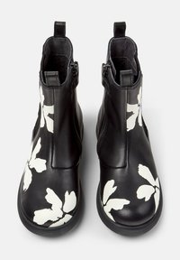 Bottines en cuir noir avec des motifs floraux blancs, fermetures éclair sur le côté et languettes à l'arrière, présentées de la vue de dessus avant.