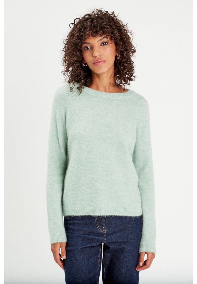 Suéter verde claro hecho de material suave, con un cuello redondo y mangas largas, combinado con jeans azul oscuro.