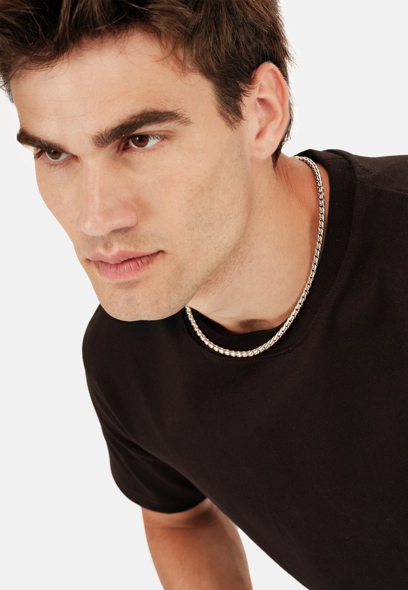 Czarna koszulka z krótkim rękawem i okrągłym dekoltem, ozdobiona srebrnym naszyjnikiem. Tło jest białe, co podkreśla koszulkę i naszyjnik.