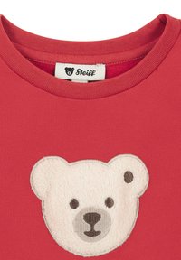 Camiseta de algodón roja con un diseño texturizado y bordado de la cabeza de un oso polar en crema y marrón. La etiqueta dice "Steiff."