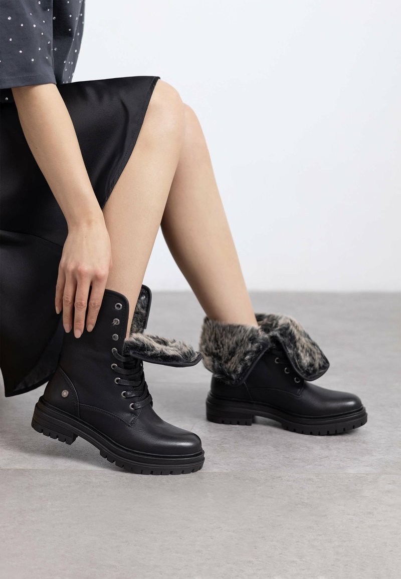 Botas de cuero negras hasta el tobillo con un cuello de piel forrado y plegable, que presentan un diseño de cordones, punta redonda y suelas de goma resistentes.