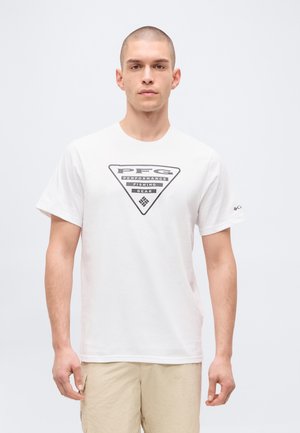 Mężczyzna w białym T-shircie z logo "PFG Performance Fishing Gear" i beżowych szortach, stojący na jednolitym jasnym tle.