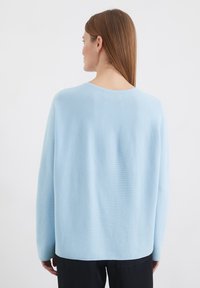 Pull léger bleu clair à manches longues avec une coupe décontractée, texture côtelée et un décolleté large ; il présente un ourlet droit et des épaules tombantes.