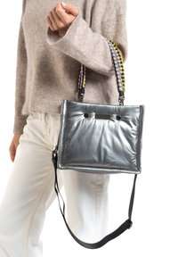 Sac à main en métal gris, de forme plate, avec une finition texturée et des surpiqûres notables. Il comprend des poignées tressées en jaune et violet.