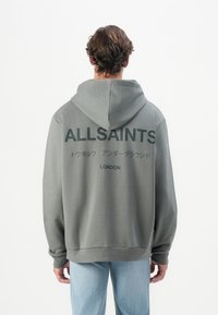 Grå hettegenser med stor svart tekst "ALLSAINTS" og japanske tegn på baksiden. Mykt stoff, avslappet passform, justerbar hette.