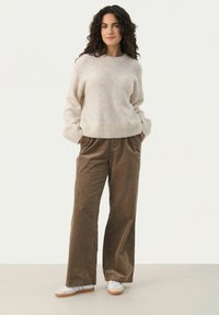 Pull en laine mélangée beige avec un ourlet côtelé. Pantalons en velours côtelé marron à jambes larges avec poches latérales. Baskets blanches avec des rayures grises.