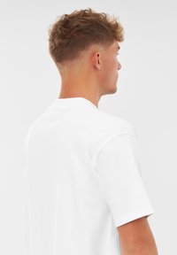 Vit bomullströja med rund hals, korta ärmar och en vanlig passform, visad från en bakvinkel som framhäver en slät textur.