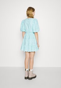 Robe bleu clair avec des manches bouffantes, en tissu en dentelle, taille cintrée et jupe évasée. Portée avec des bottes à lacets roses claires et des chaussettes blanches.
