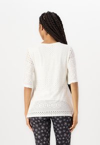 Witte korte mouwen top met geperforeerd ontwerp, met gevarieerde cirkelvormige patronen. Losse pasvorm, zachte textuur, gecombineerd met zwarte broek met bloemenprint.