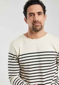 Camicia a maniche lunghe a righe realizzata in tessuto morbido. Colore crema con righe orizzontali blu navy. Presenta un collo rotondo e maniche aderenti.