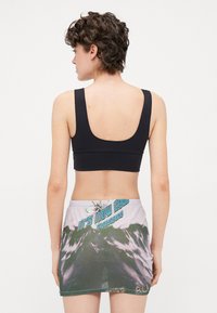 Top corto negro sin mangas con tirantes anchos, combinado con una falda corta que presenta un diseño de ondas y detalles en texto en azul y verde.