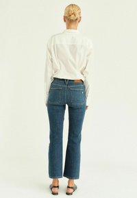 Tmavě modré džíny s mírným rozšířením, texturovaný denim a dvě zadní kapsy. V kombinaci s bílou košilí s dlouhým rukávem a černými sandály.