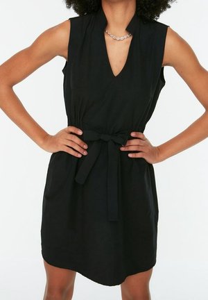 Sort kjole med V-udskæring, ærmeløs design og bindebånd i taljen. Glat tekstur, knælængde, med sidelommer for funktionalitet.