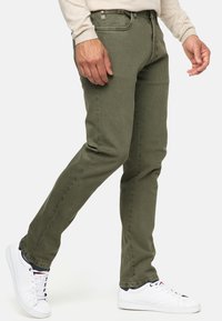 Jeans verde oliva con un ajuste slim, fabricados con una mezcla de algodón. Presentan bolsillos delanteros, cierre de botón y acentos de diseño minimalista.