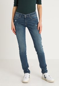 Tunna denimjeans i medelblå med lätt slitage. Har en klassisk femficksdesign och en dragkedja med knappstängning.