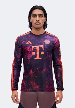 Mand med mørkt hår bærer langærmet Bayern München fodboldtrøje i lilla og rød mønster med T-Mobile-logo og Adidas-striber på ærmerne.