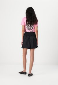 T-shirt rose avec un graphique de boule à facettes et le texte "Party", associé à une jupe noire évasée. Chaussures plates noires avec des découpes.