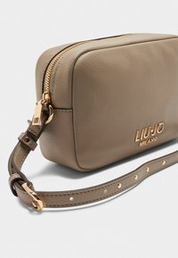 Beige lædertaske med rektangulær form, der har en gylden lynlås, LIU JO Milano-logo og en justerbar rem med nagle-accenter.