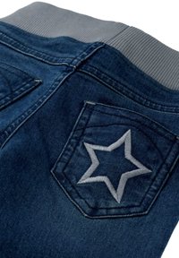 Jeans de mezclilla con un lavado azul oscuro, que cuentan con una cinturilla acanalada gris y un bolsillo trasero decorado con un bordado de estrella plateada.