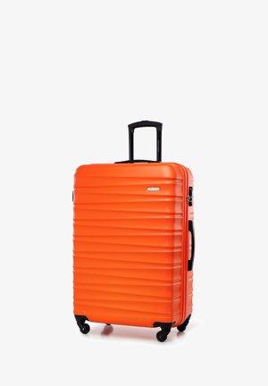 Maleta rígida de color naranja brillante con cuatro ruedas giratorias y asa negra retráctil, de pie sobre un fondo blanco.