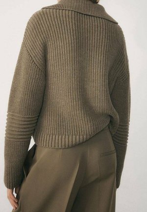 Persona che indossa un maglione morbido a coste verde oliva con maniche lunghe e pantaloni verde oliva a vita alta, vista da dietro.