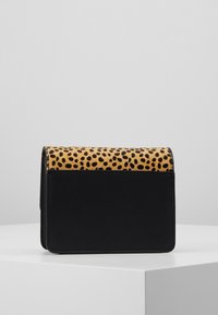 Borsa a tracolla in pelle nera con una patta in tessuto giallo a pois. Design compatto con una forma strutturata e una texture liscia.