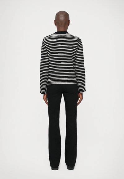 Maglione a righe bianco e nero con maniche lunghe e scollo rotondo, abbinato a pantaloni neri, visto dalla schiena su uno sfondo bianco.