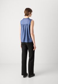 Κοντομάνικο μπλέ μπλούζα χωρίς μανίκια με μαζεμένη πλάτη, στρογγυλή λαιμόκοψη, μαλακή υφή, σε συνδυασμό με μαύρα παντελόνια και επίπεδες παπούτσια. Απλός σχεδιασμός, χωρίς σχέδια.