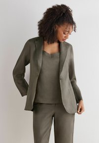 Linne kostym i olivgrön med en blazer med snedskurna slag, en v-ringad topp och skräddarsydda byxor. Tyget har en strukturerad finish.