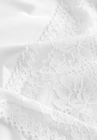Material de dantelă albă cu modele florale și detalii intricate. Textură netedă cu margini zimțate și detalii fine.