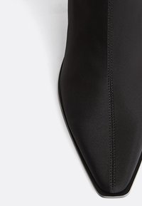 Stivaletto nero con punta a punta realizzato in tessuto liscio, con dettagli di cuciture sottili e un design elegante e minimale senza elementi metallici visibili.