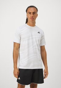 Valge sportlik T-särk lainemustriga ja must Adidas'i logo vasakul rinnal, koos mustade lühikestega, millel on valged äärised.