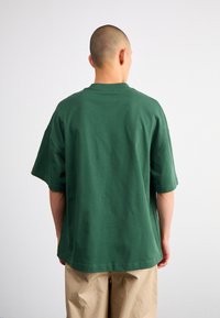 Camiseta de algodón verde con un corte relajado, mangas cortas y cuello redondo. La tela parece suave y lisa, sin patrones visibles.