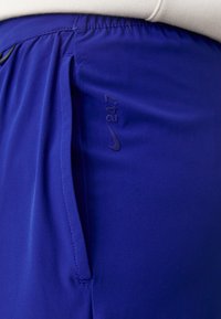 Nike 247 trenirke u vibrantnoj plavoj tkanini imaju gladak tekstur, elastičan pojas, bočne džepove i suptilan detalj s logom.