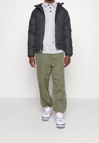 Svart vadderad jacka, grå pikétröja, olivgröna träningsbyxor och vita sneakers med röda och grå accenter.