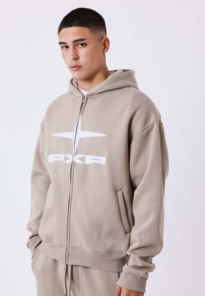 Khakifarbene Zip-Hoodie aus weichem Stoff mit einem großen weißen Logo. Er hat eine Fronttasche und eine Kapuze mit Kordelzug sowie gerippten Bündchen.