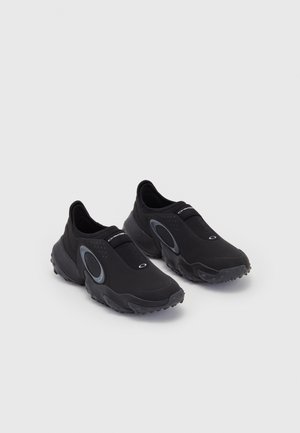 Črne slip-on športne copate z teksturiranim zgornjim delom in gumijastim podplatom. Imajo sivo krožno dekoracijo in elastični trak čez gleženj za boljše prileganje.