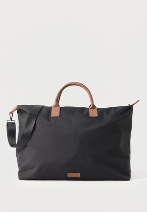 Duża czarna torba podróżna z brązowymi skórzanymi uchwytami i odpinanym czarnym paskiem na ramię na białym tle.