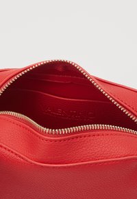 Röd läderväska inuti med en metallisk dragkedja. Inuti har den en slät textur och diskret präglad logotyp.