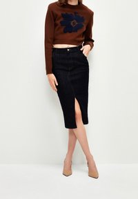 Femme portant un pull court marron avec un motif floral bleu marine, une jupe midi en denim foncé avec une fente à l'avant, et des talons pointus beige.