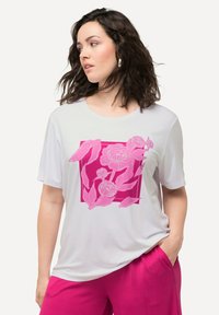 La camiseta de manga corta de color gris claro presenta un diseño floral rosa en un cuadrado, combinada con pantalones cortos plegados rosa. Textura suave, corte relajado.