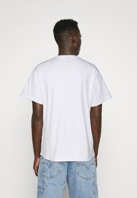 White cotton t-shirt with a relaxed fit, short sleeves, and a classic crew neck, displayed from the back against a plain background.