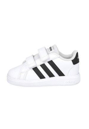 Zapatilla atlética blanca con diseño de tres rayas negras y correas de Velcro. Fabricada en material sintético, cuenta con una suela de goma y un cuello acolchado.