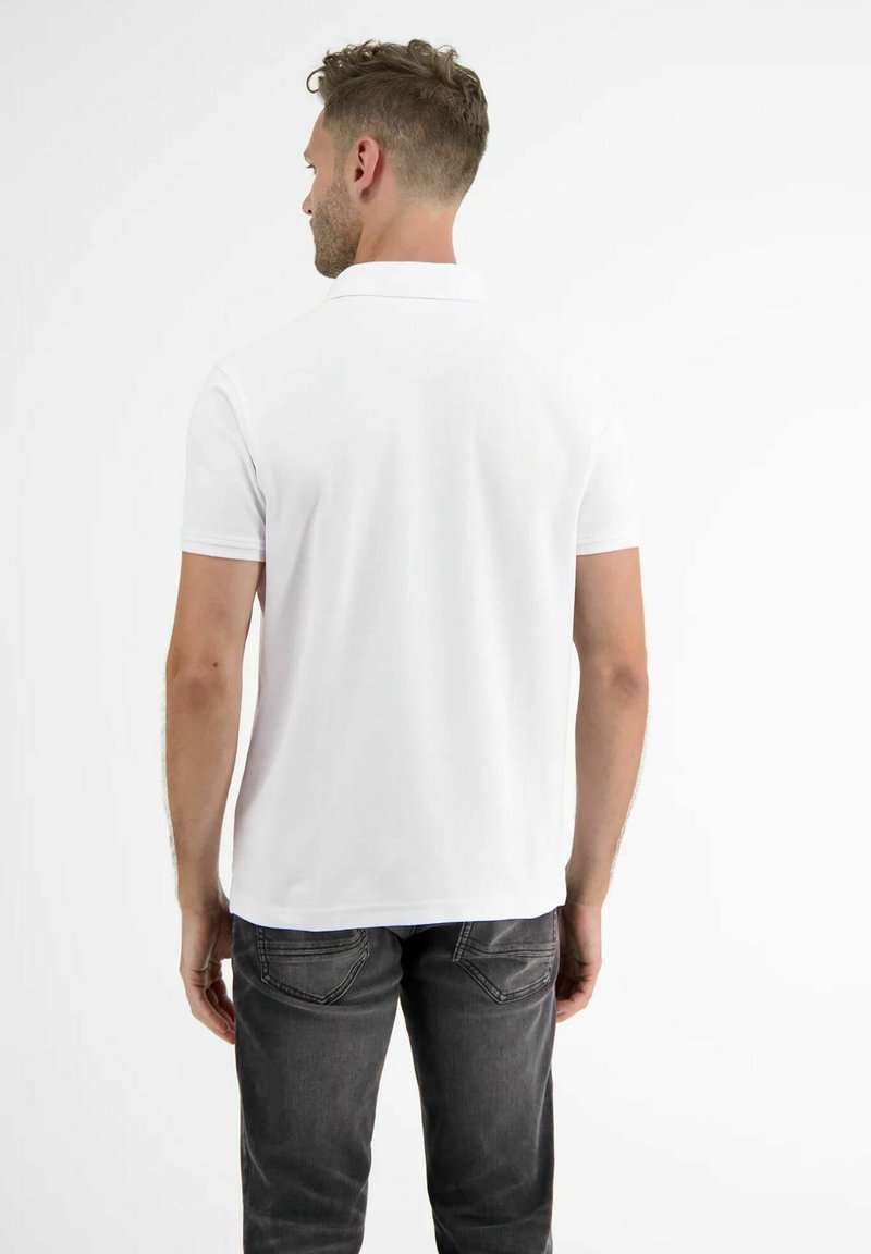 Man facing away wearing a plain white short-sleeve polo shirt and dark gray jeans against a white background.