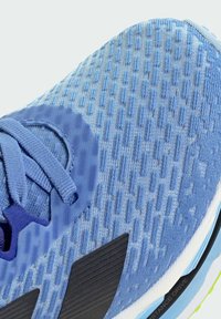 Light blue athletic shoe with textured fabric upper, black accents, and laces. Features a cushioned sole and hexagonal pattern on the material.