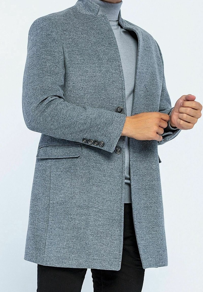 Cappotto grigio in misto lana con colletto alto, due bottoni e tasche laterali. Tessuto liscio con vestibilità su misura e design strutturato.