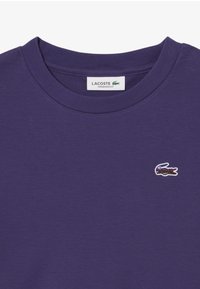 T-shirt oversize viola in cotone, con scollo rotondo e logo del coccodrillo Lacoste ricamato sul lato sinistro del petto.